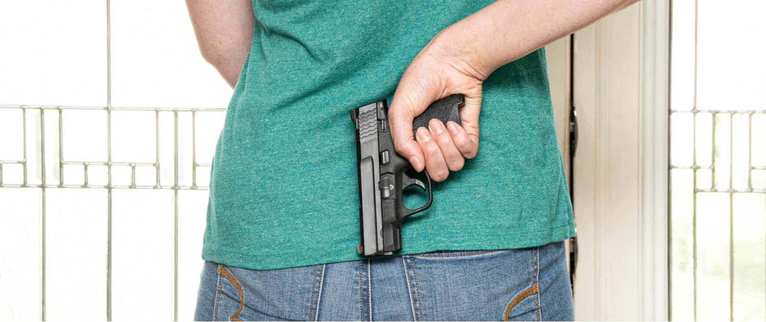 a woman holding a handgun behind her Back in a home defense scenario